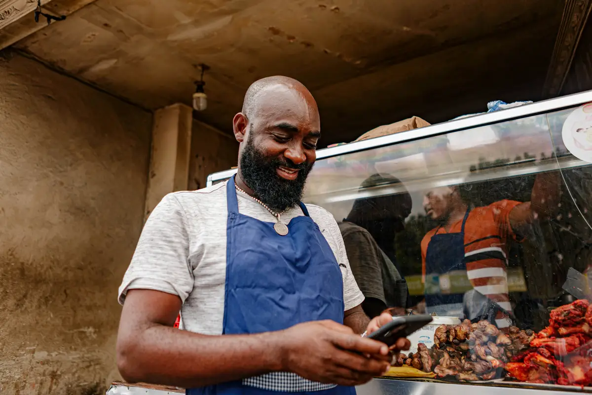 A food-stall owner smiling while checking orders on his phone.