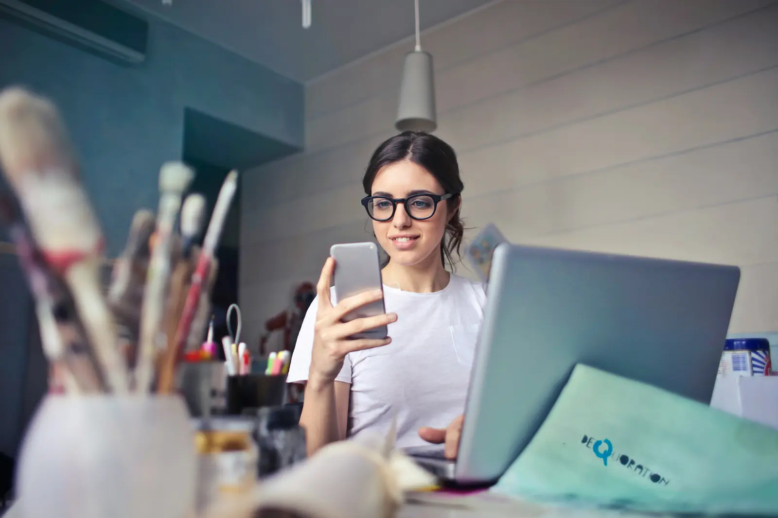 A business owner answering messages on her phone in front of a laptop.